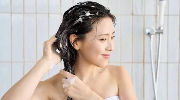 Woman washing her hair with shampoo before applying a hair mask as part of a cleansing routine